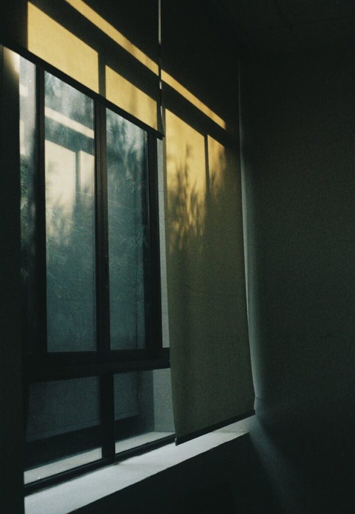 Warm sunlight filters through roller blinds, casting shadows indoors.