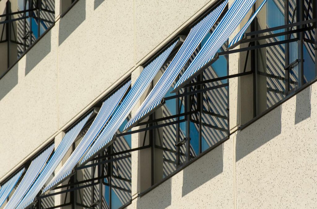 Close-up of contemporary building facade with blue and white striped awnings providing shade.
