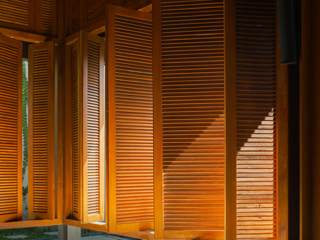 Sunlight casting artistic shadows on wooden shuttered windows creating a warm, aesthetic interior.