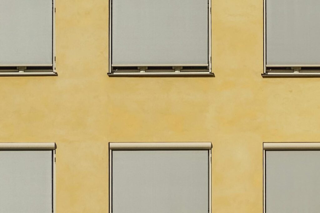 Modern building facade in Oslo with minimalist ochre walls and closed blinds creating a geometric pattern.